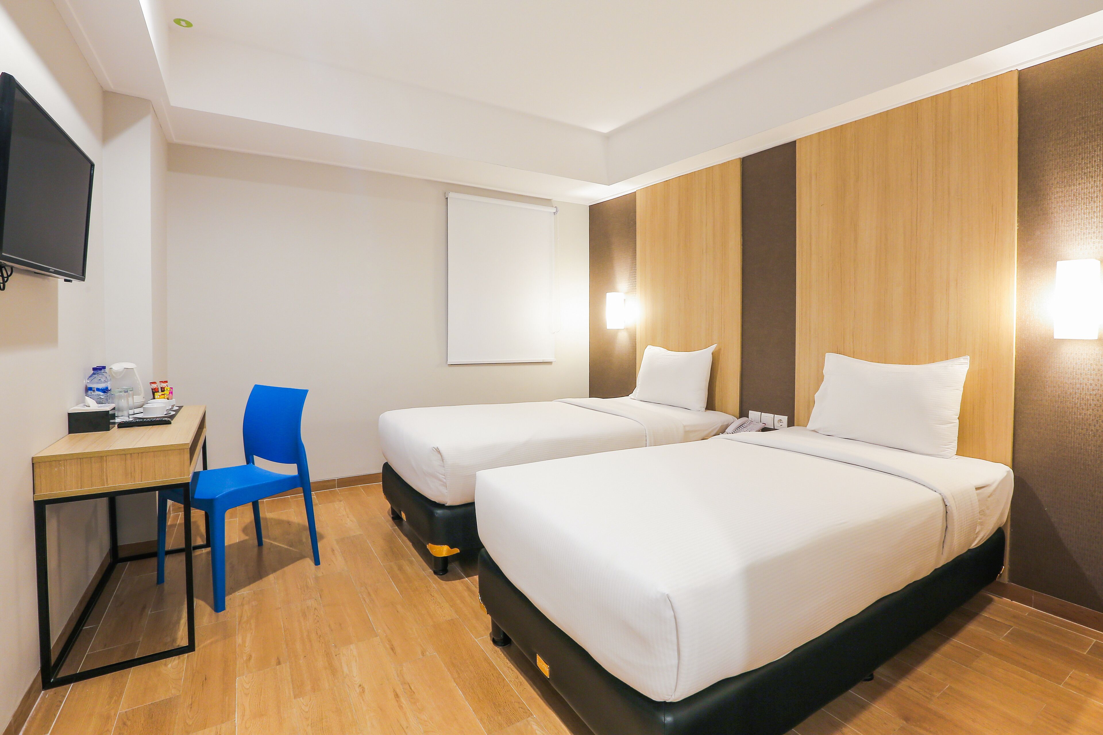 Une chambre d’hôtel avec deux lits, un bureau, une chaise et un téléviseur fixé au mur.