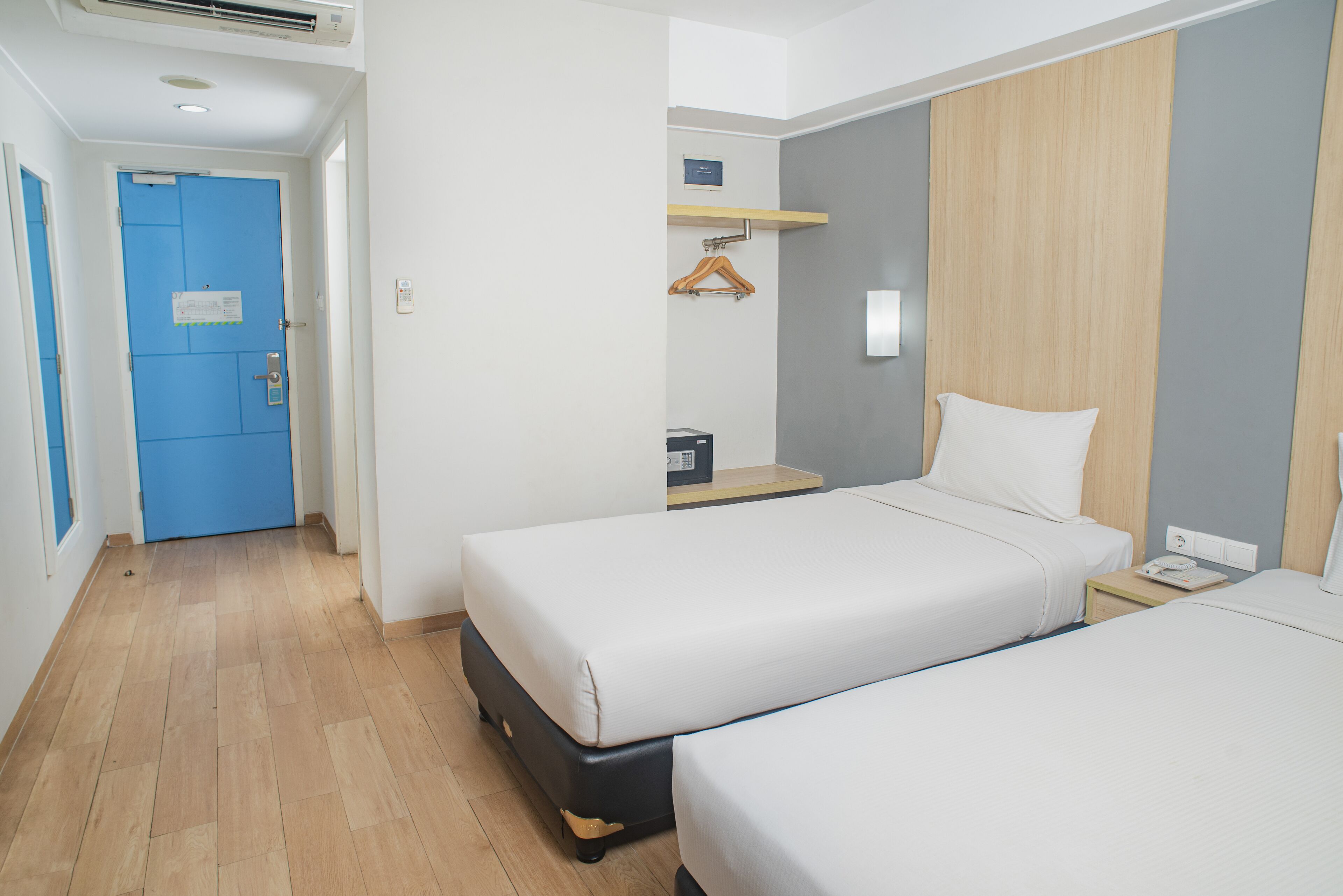 Une chambre d’hôtel avec deux lits, une armoire en bois, une porte bleue et une petite table avec un porte-manteau suspendu.