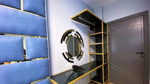 A modern room with a blue padded wall, a glass console table with a black top, a gold-framed mirror, and a wooden door. - Orange Airport Hotel (Istanbul)