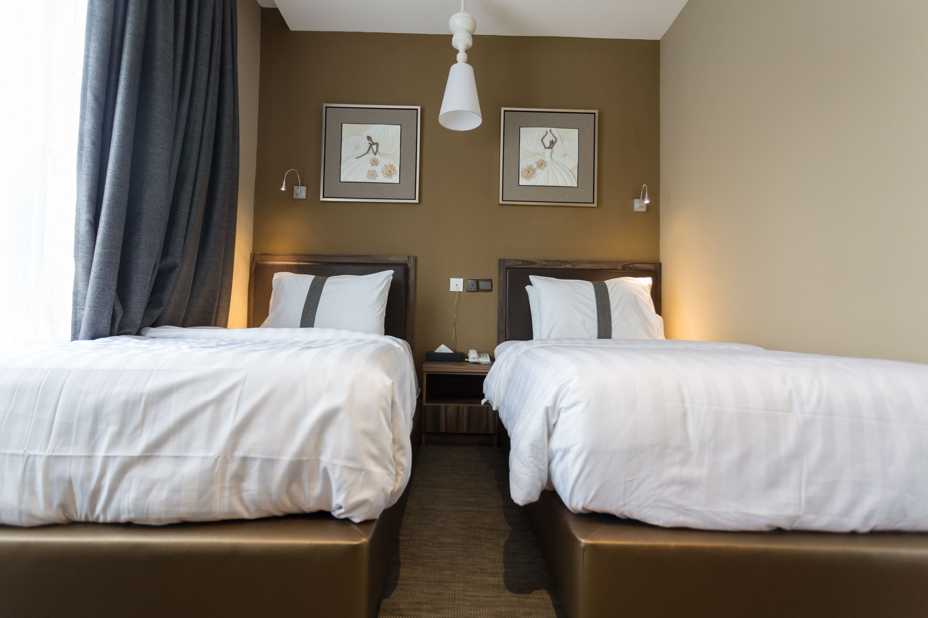 A hotel room with two single beds, a nightstand, and a wall-mounted lamp.