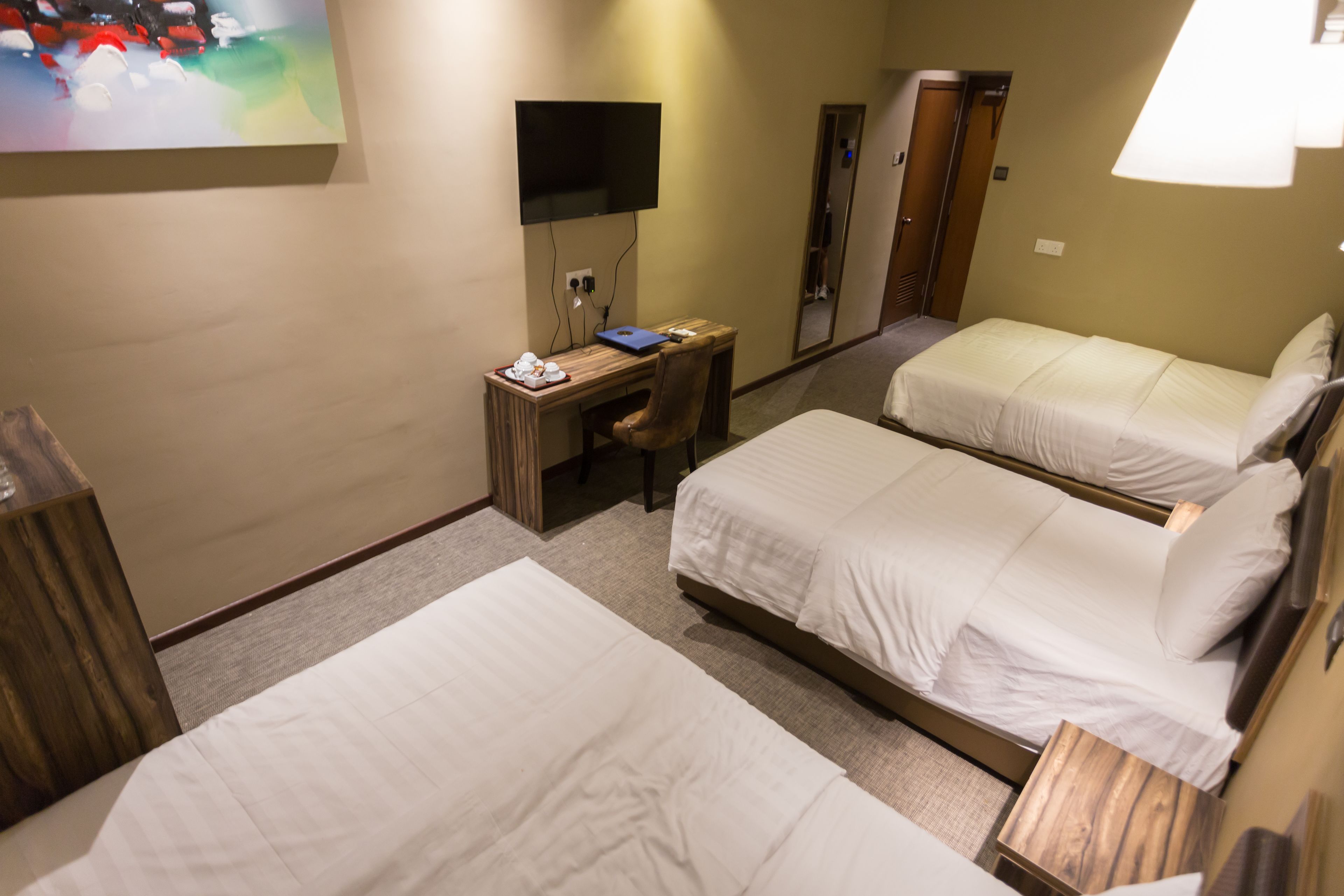 A hotel room with two beds, a desk with a laptop, a TV, and a mirror.