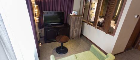 A hotel room with a green sofa, a television on a wooden cabinet, a small round table, and a mirror on the wall.