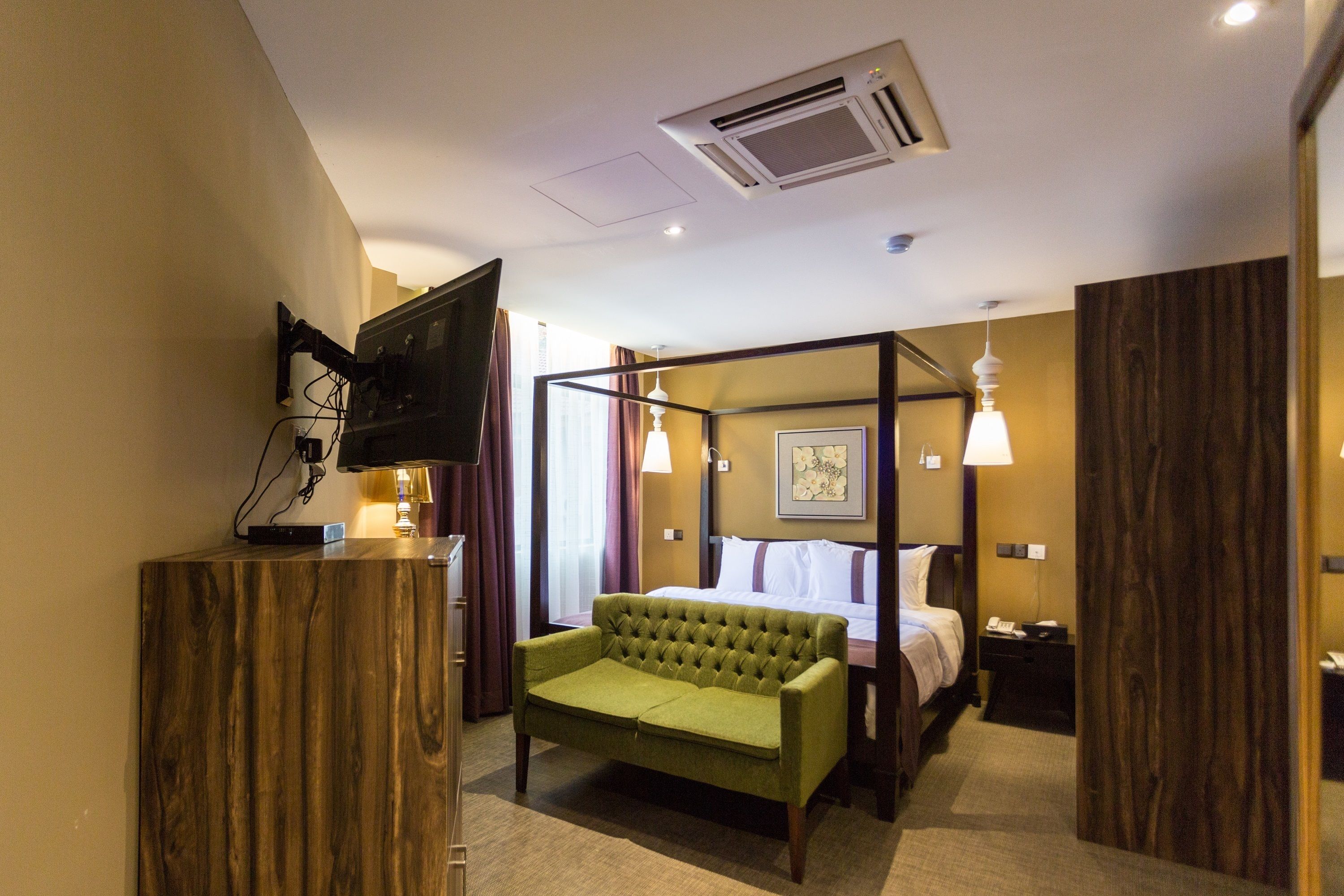 Ein Hotelzimmer mit einem grünen Sofa, einem Himmelbett, einem Flachbildfernseher an einem Holzkabinett und einem Nachttisch mit Lampe.