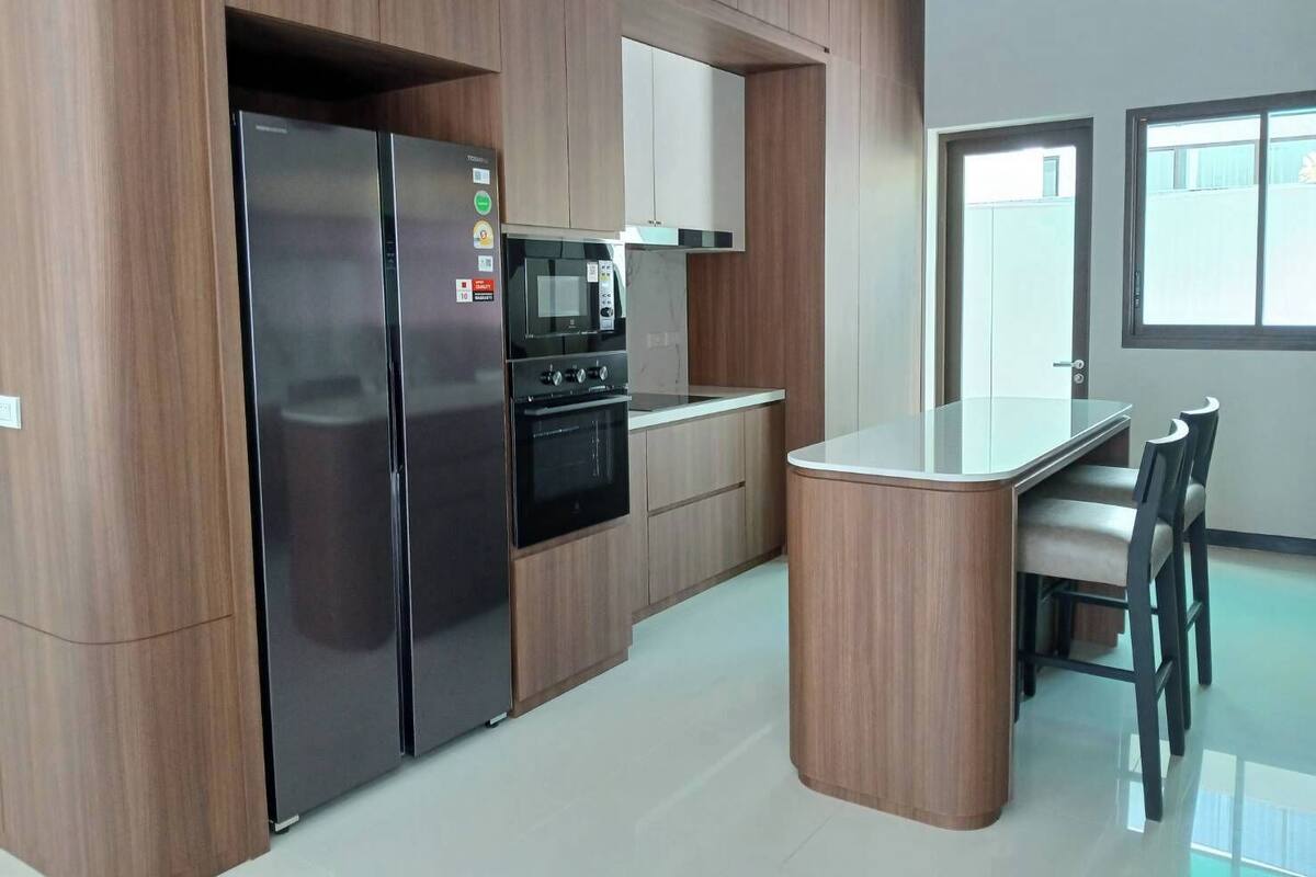 A modern kitchen with a built-in refrigerator, oven, microwave, and a central island with chairs.