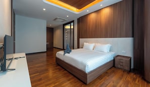 A modern hotel room with a large bed, a desk with a computer, and a view of the hallway.