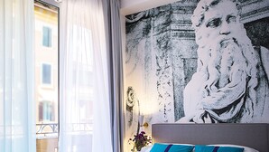 A hotel room with a large bed, a window with sheer curtains, and a wall mural. - Milizie 76 Gallery (Rome)