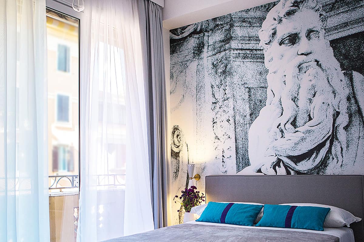 A hotel room with a large bed, a window with sheer curtains, and a wall mural.