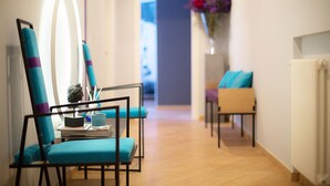 A hallway with two blue chairs, a small table with a book and a glass, and a vase with flowers. - Milizie 76 Gallery (Rome)