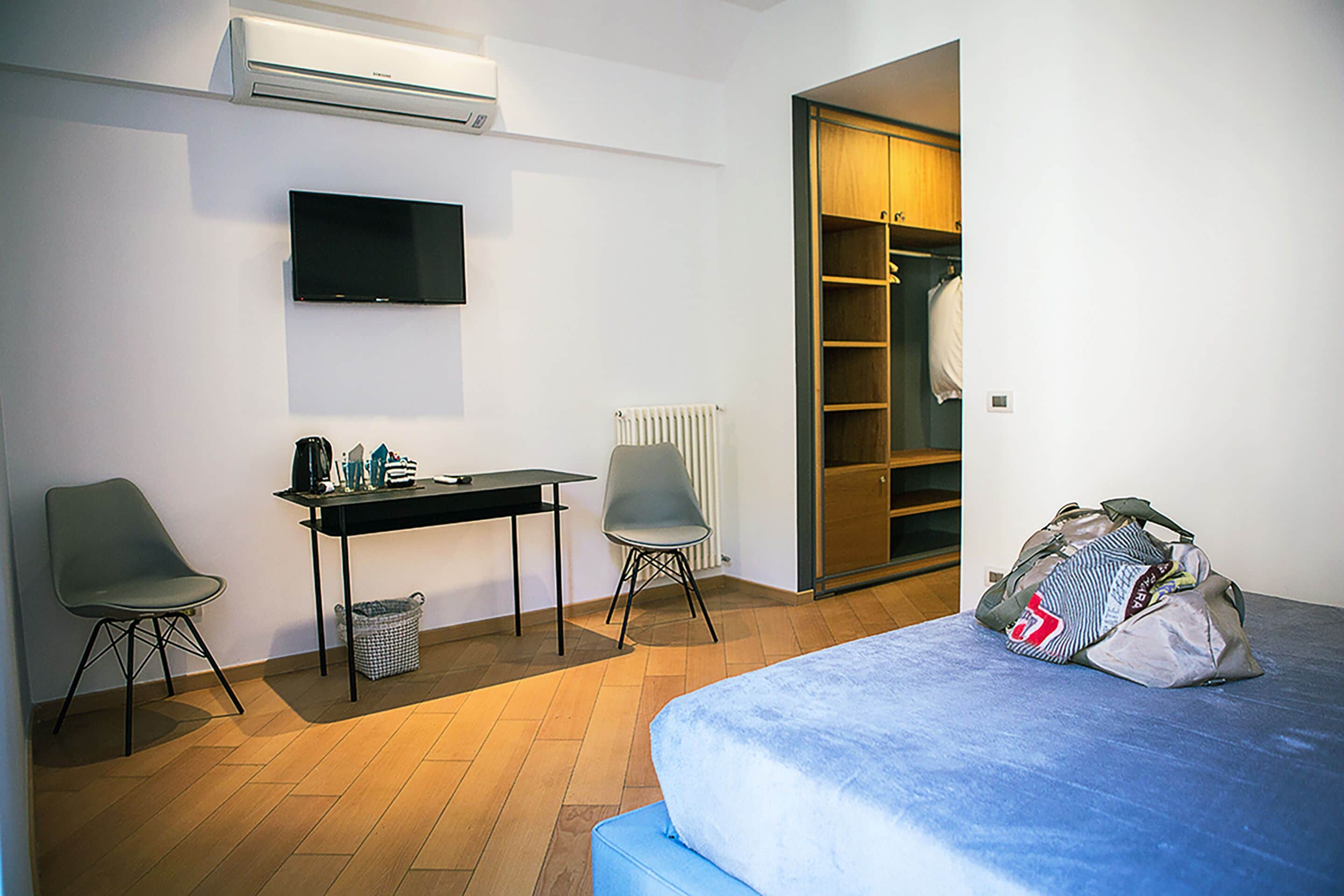 A hotel room with a bed, a desk with a chair, a television, and a wardrobe.
