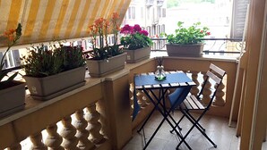 A balcony with a table and chairs, potted plants, and a striped awning. - Milizie 76 Gallery (Rome)