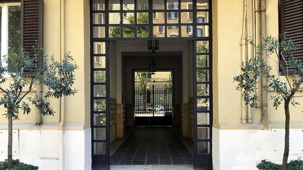 A building entrance with a tiled floor, a black gate, and two trees on either side. - Milizie 76 Gallery (Rome)