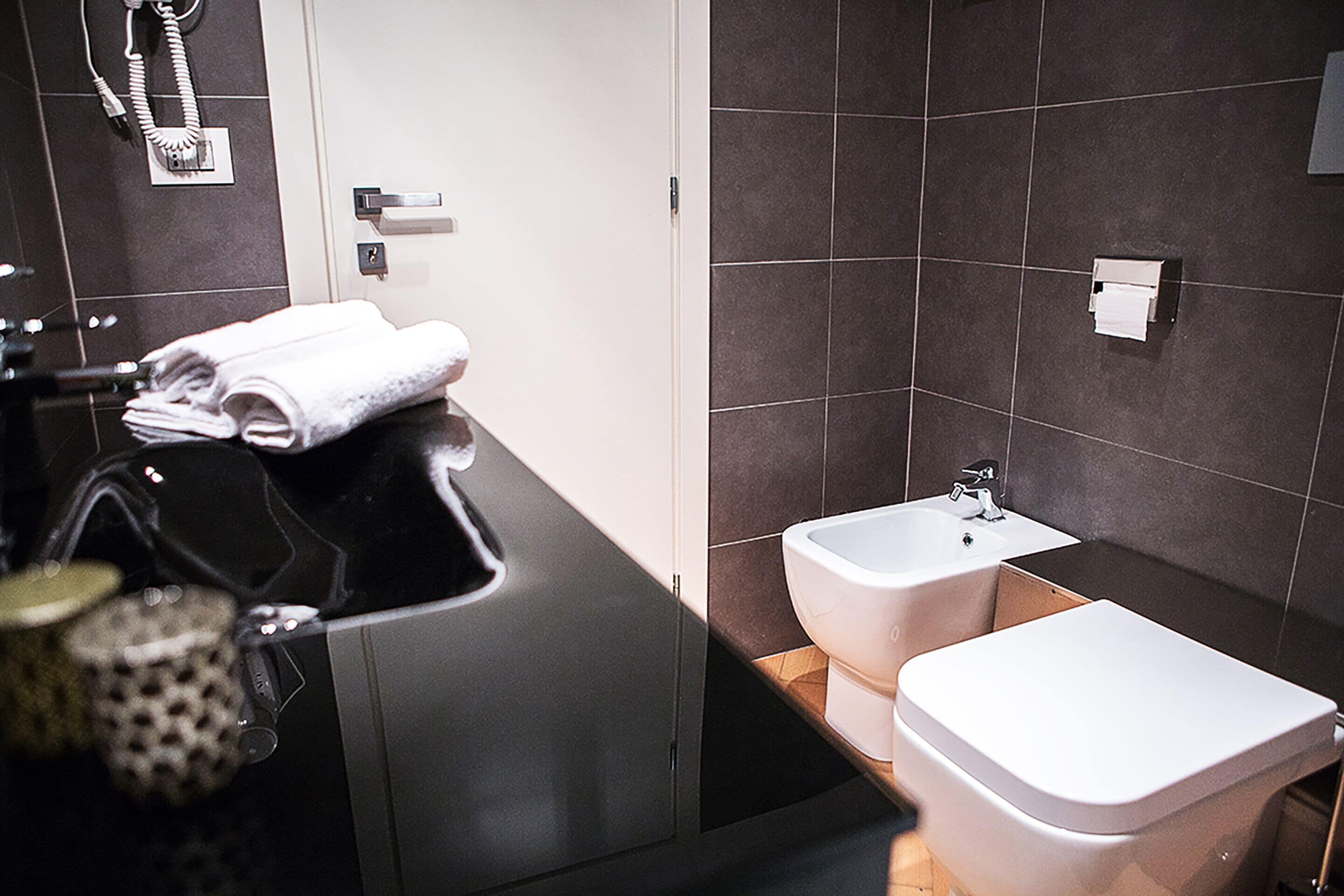 A modern bathroom with a black countertop, a white sink, and two bidets.