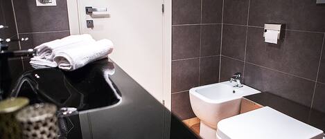 A modern bathroom with a black countertop, a white sink, and two bidets.