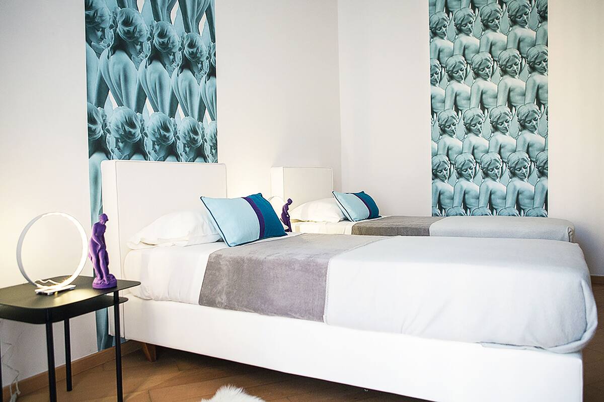A modern bedroom with a large bed, bedside tables, and a wall-mounted mirror.