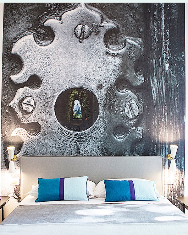A bedroom with a large bed, two blue pillows, and a wall mural with circular patterns.