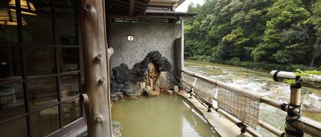 A traditional Japanese onsen with a wooden structure, a stone wall, and a view of a flowing river.