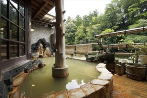 A traditional Japanese onsen with a stone bath, wooden pillars, and a view of lush greenery. - Hazu Bekkan (Shinshiro)