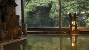 Una piscina interior tranquila con una escultura de madera y una escalera, reflejando árboles a través de una ventana.