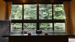 Una habitación con un amplio ventanal que da a un bosque. Hay una mesa de madera con una tetera y tazas encima.