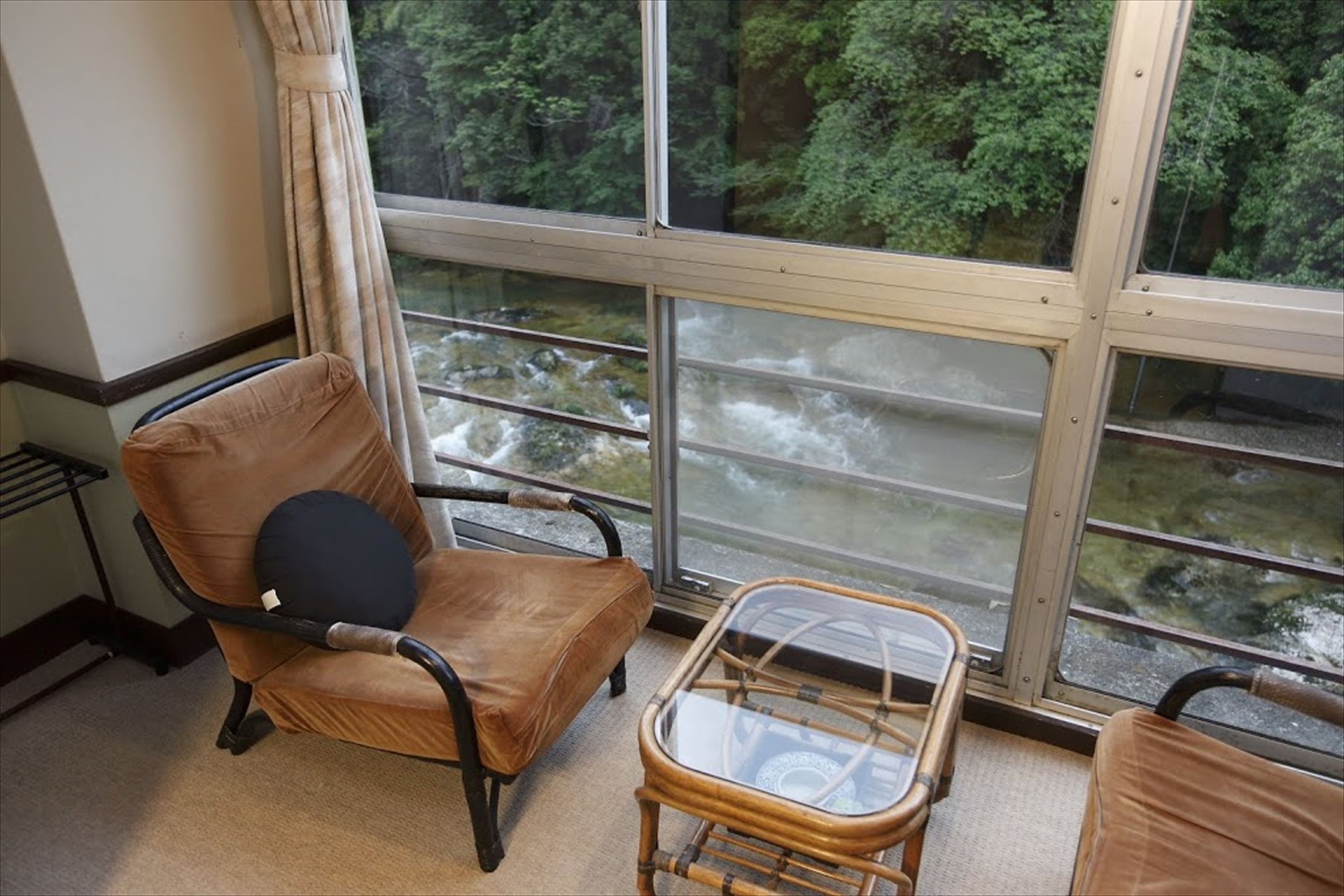 A room with a large window overlooking a river, a brown leather chair, and a small glass-top table.