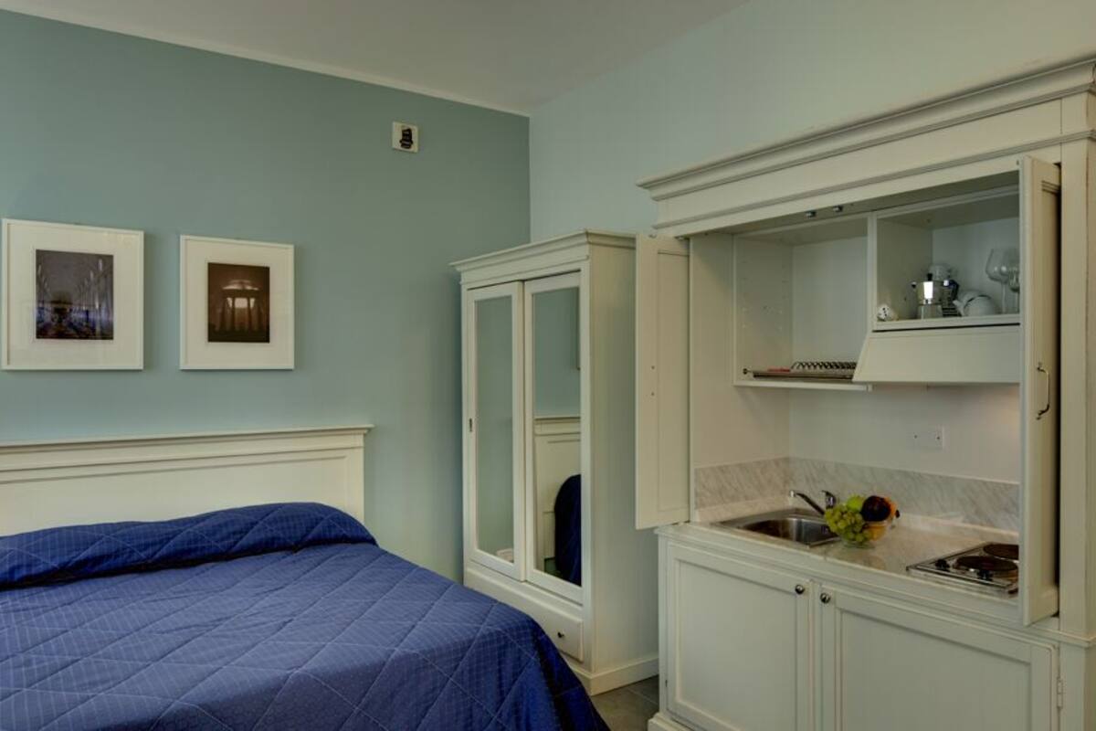 A hotel room with a bed, a nightstand with a lamp, a mirror, and a cabinet with a sink and countertop.