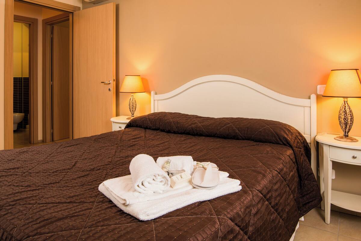 A neatly made bed with a brown quilt, white headboard, and two bedside lamps.
