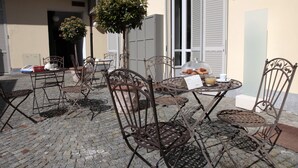 Un café al aire libre con sillas y mesas de metal, una planta en maceta y una cúpula de cristal que exhibe comida.