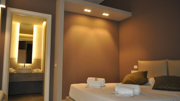 Habitación de hotel con cama, lámparas de noche, baño con lavamanos y espejo.