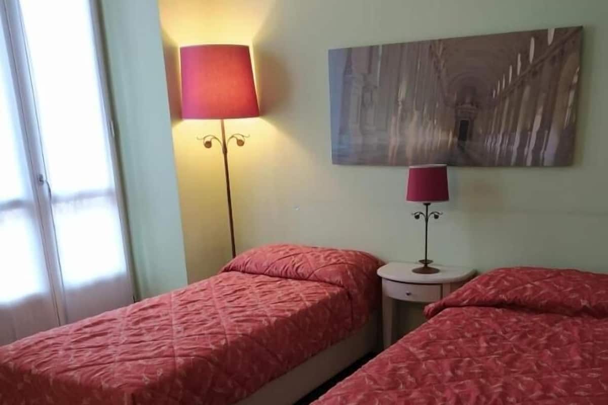 A room with two beds, a lamp, and a painting on the wall.