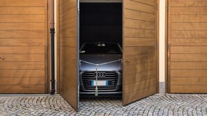 Un coche estacionado en un garaje con puertas de madera y piso de adoquines.