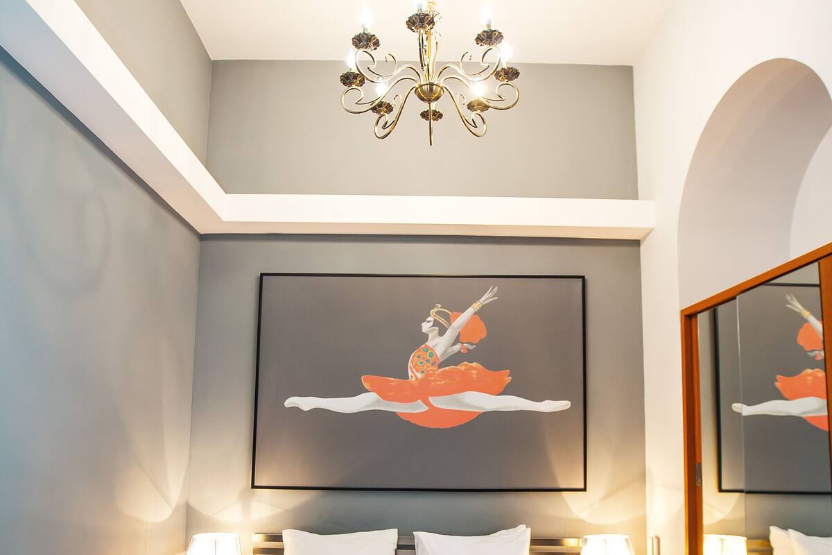 A hotel room with a large bed, a chandelier, a framed artwork above the bed, and a mirror on the wall.