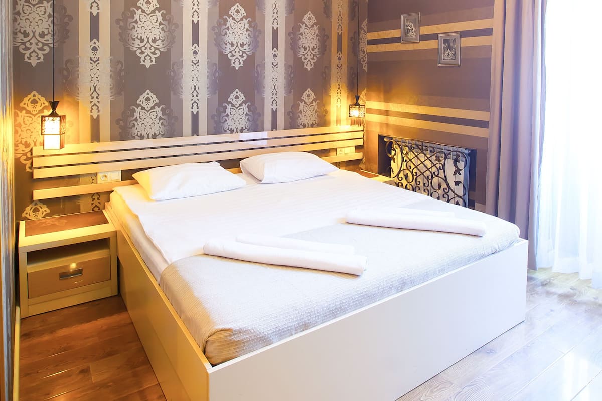 Ein modernes Schlafzimmer mit einem großen Bett, Holzboden, dekorativer Tapete und einem Chandelier.