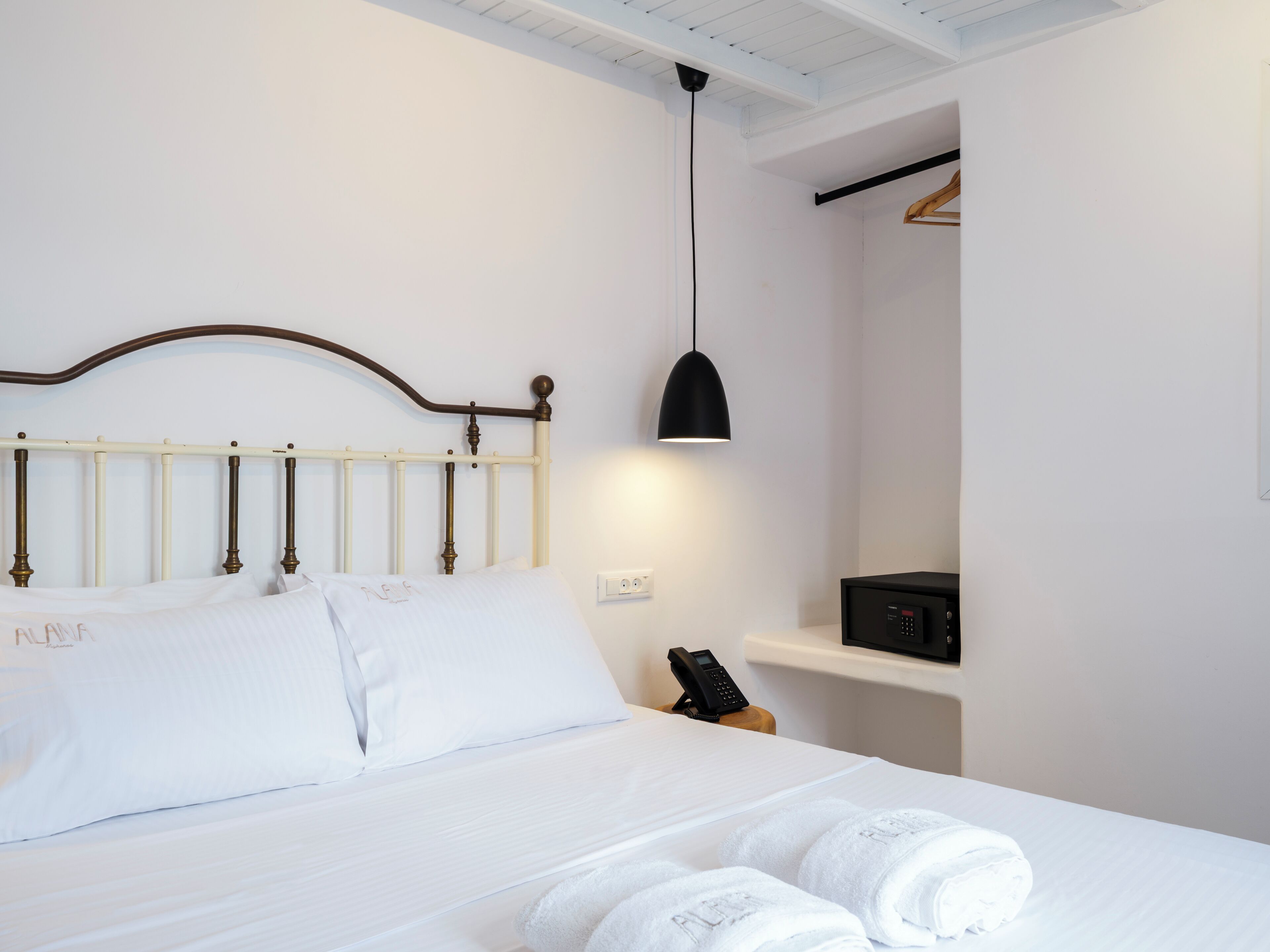 A neatly made bed with white linens and a wooden headboard, a bedside table with a phone, and a black pendant light.
