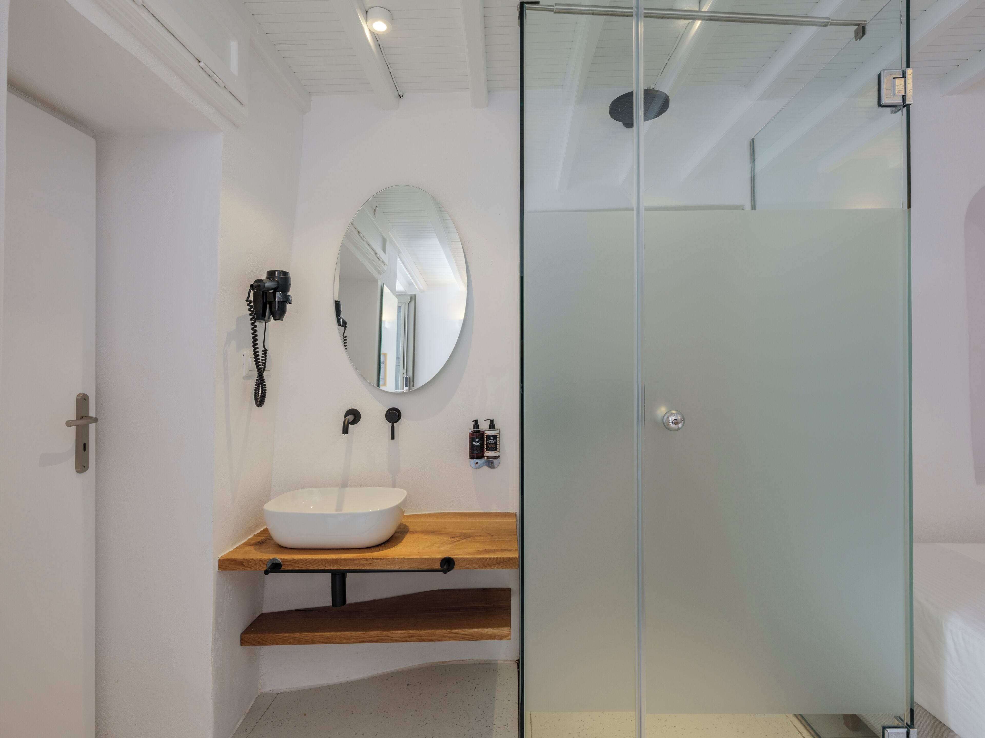 A modern bathroom with a glass-enclosed shower, a white sink with a wooden countertop, and a wall-mounted mirror.