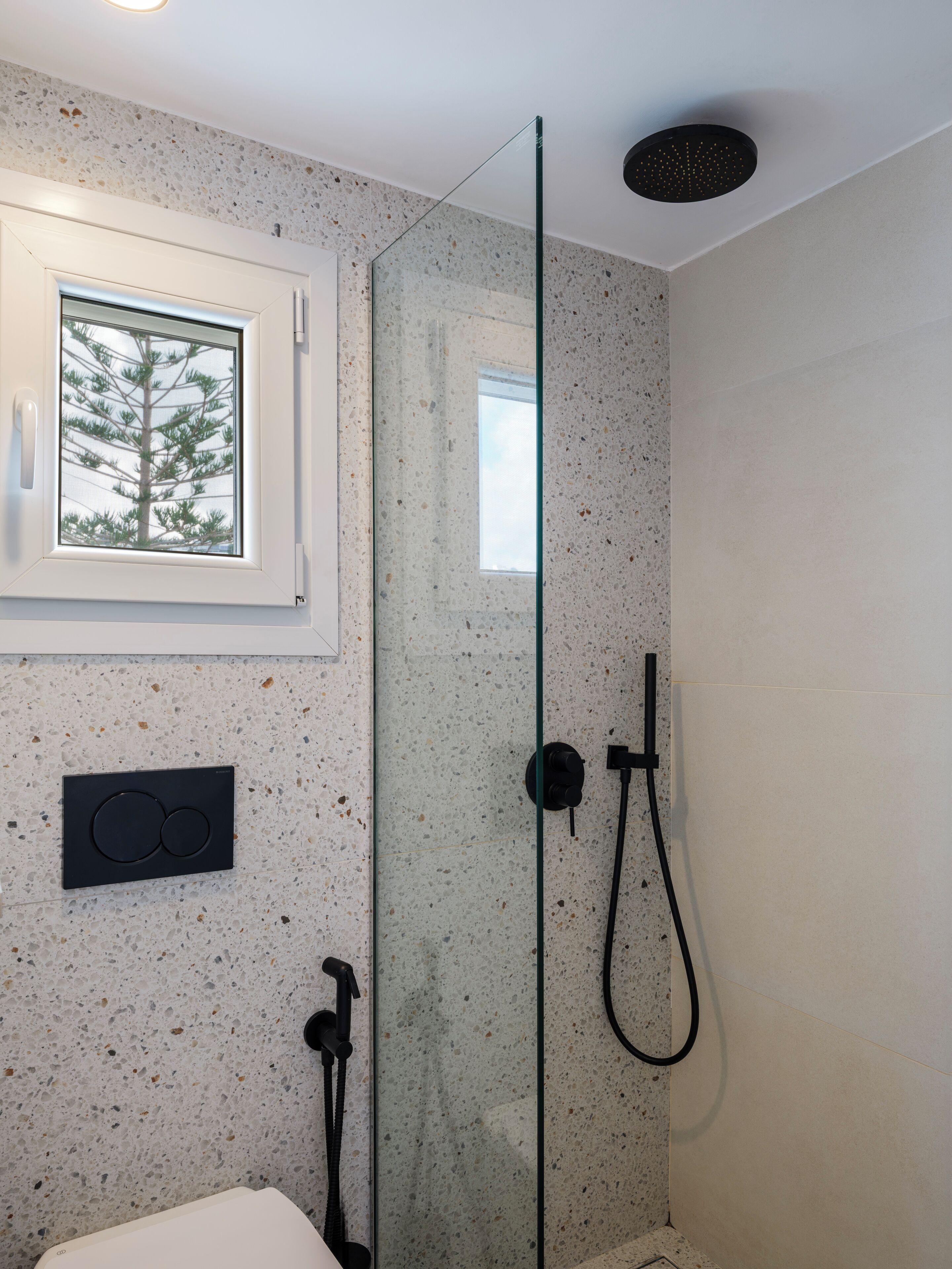 Une salle de bain moderne dotée d’une douche à parois de verre, d’une fenêtre donnant sur la verdure et d’un panneau de commande intégré.