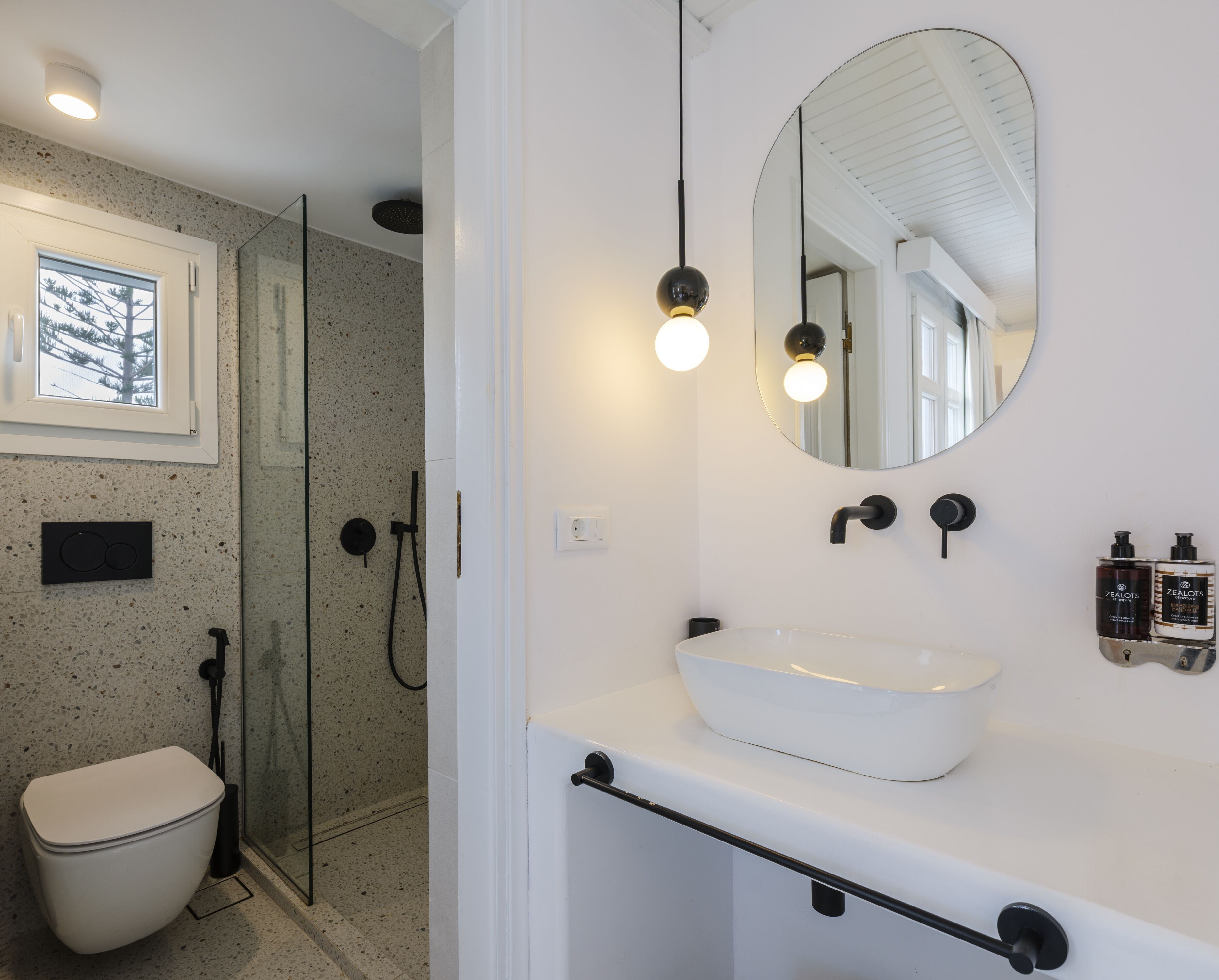 Un bagno moderno con un lavandino bianco, uno specchio rotondo e una zona doccia.