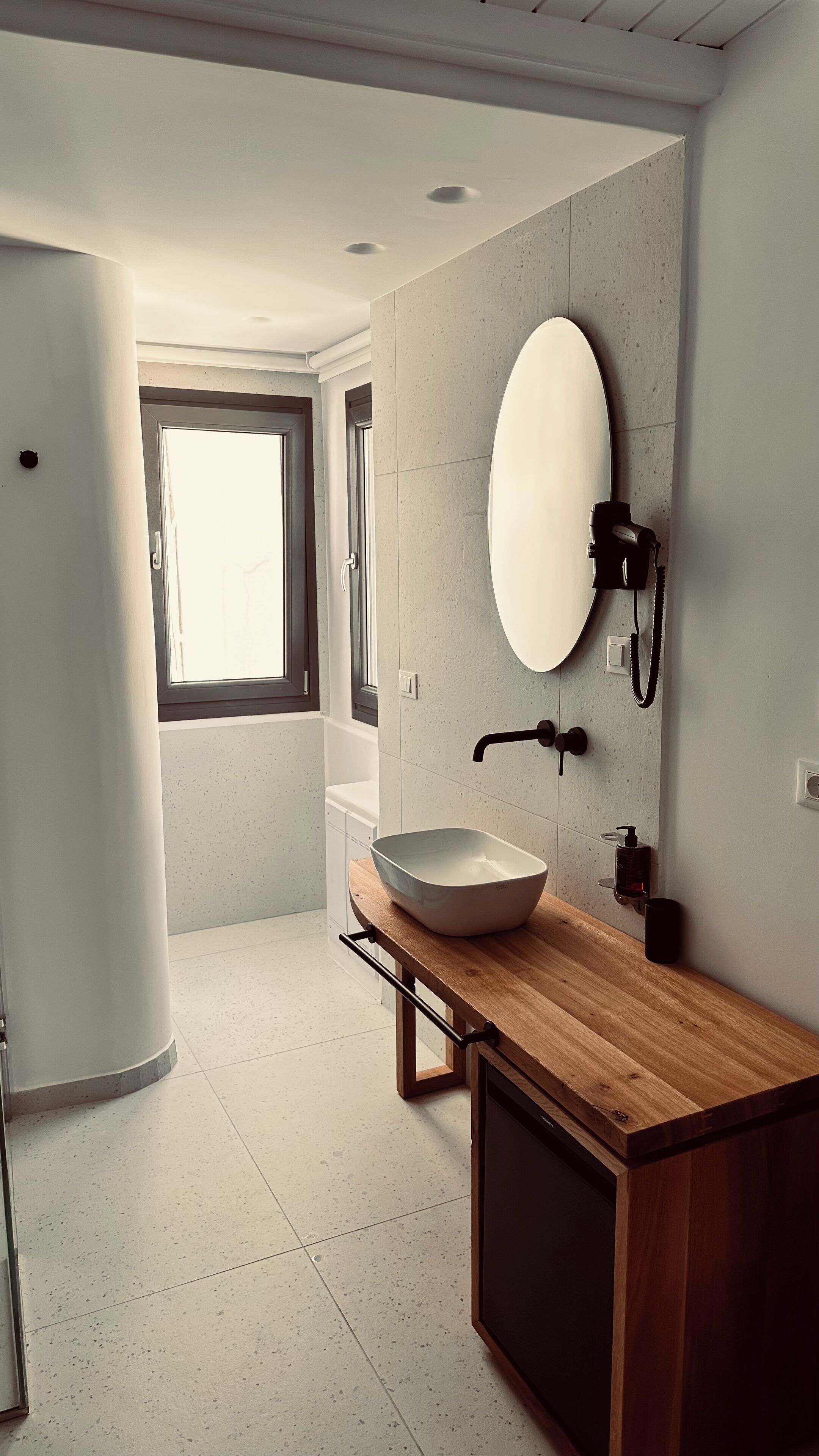 Un baño moderno con un espejo ovalado grande, un tocador de madera y un lavamanos blanco.