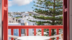 A balcony with a white table and chairs, overlooking a coastal town with white buildings and a clear blue sky. - Alana Mykonos (Mykonos)