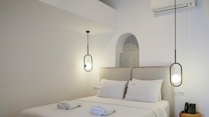 A modern hotel room with a neatly made bed, a small wooden side table with a phone, and a wall-mounted air conditioner. - Alana Mykonos (Mykonos)