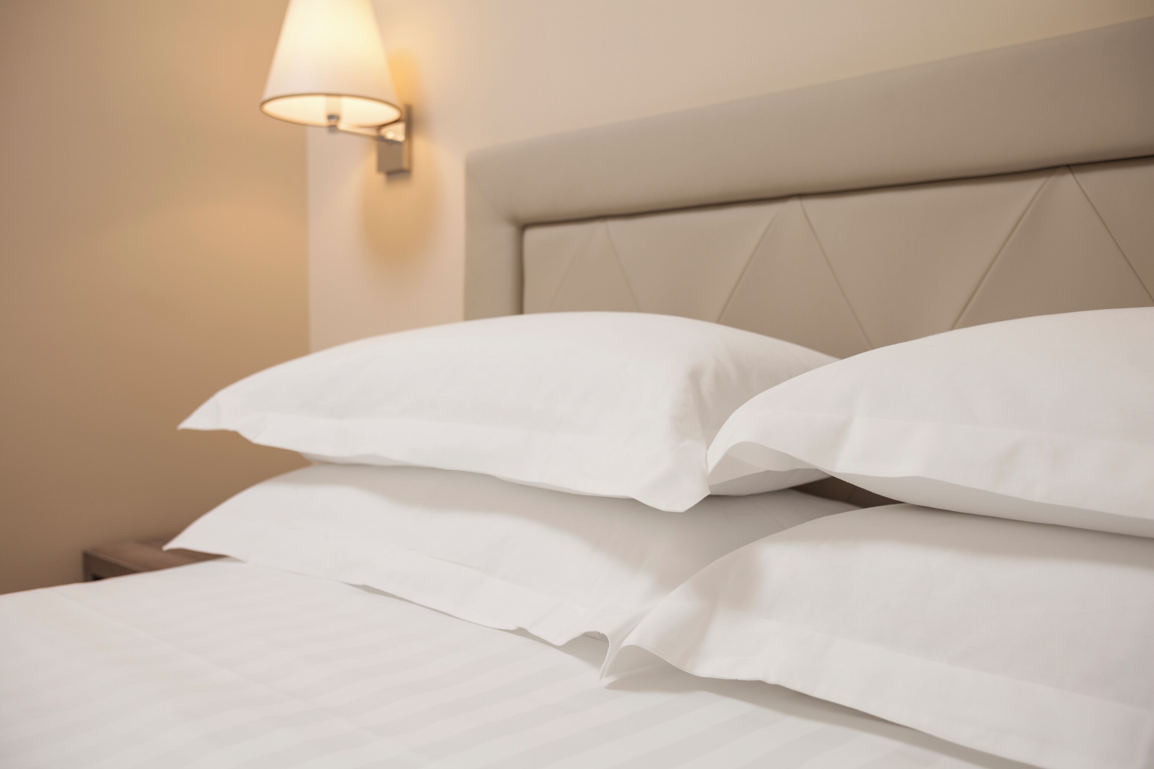 A neatly made bed with white linens and a headboard with a diamond pattern.