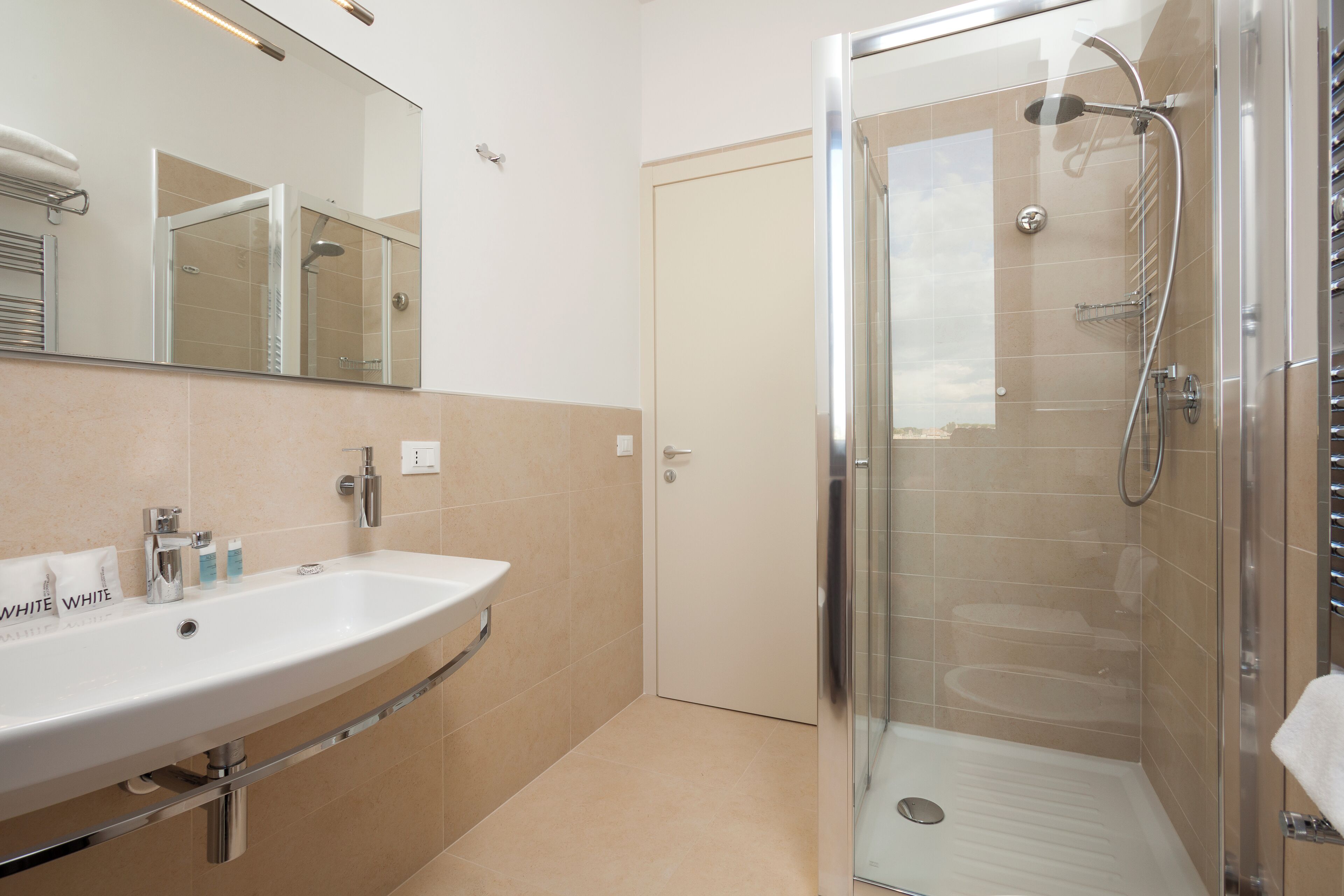Ein modernes Badezimmer mit einem großen Waschbecken, einer Duschkabine aus Glas und einer Tür zu einem weiteren Raum.