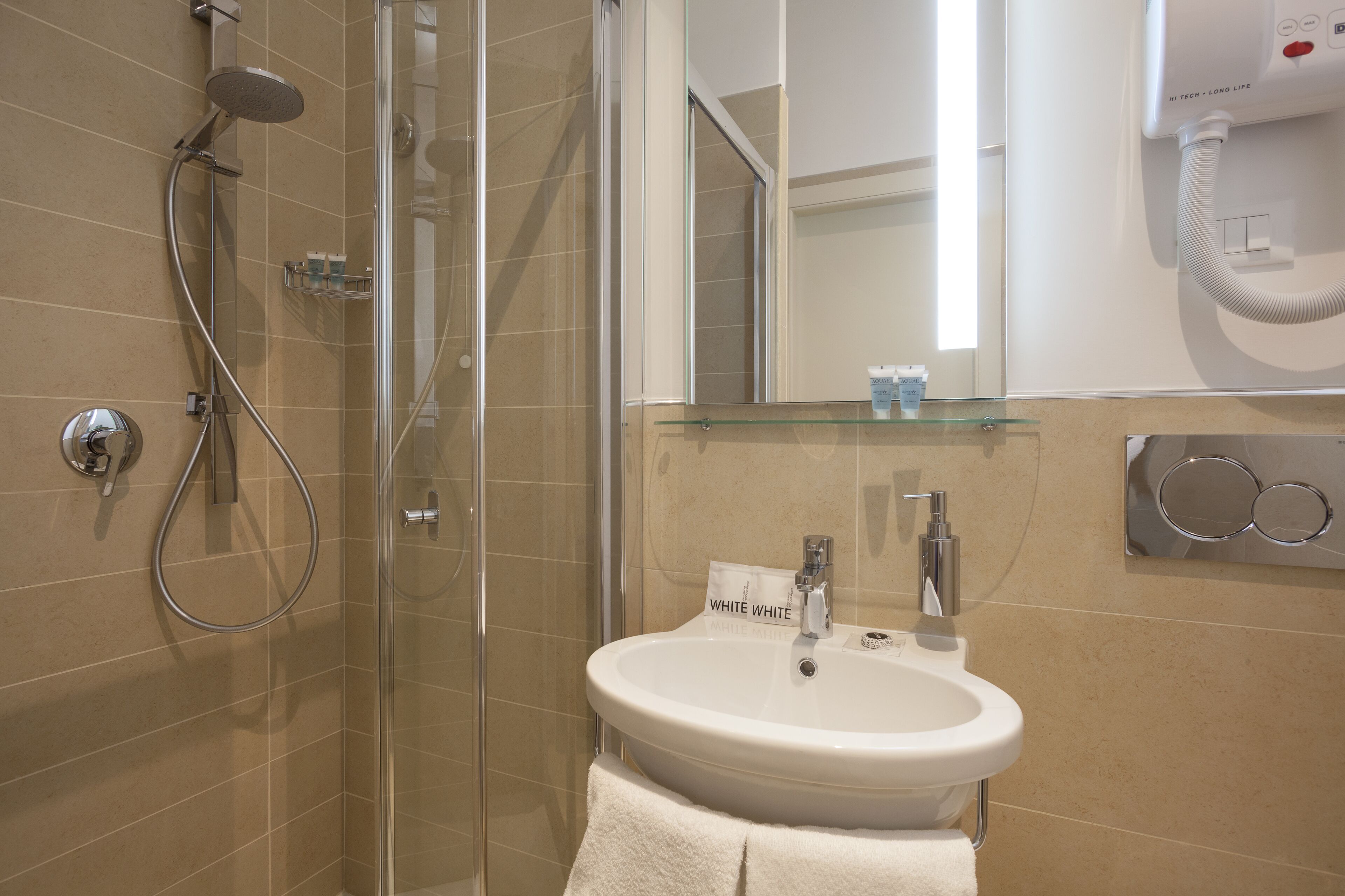 Uma casa de banho moderna com cabine de duche em vidro, lavatório branco com espelho em cima e secador de cabelo fixado na parede.