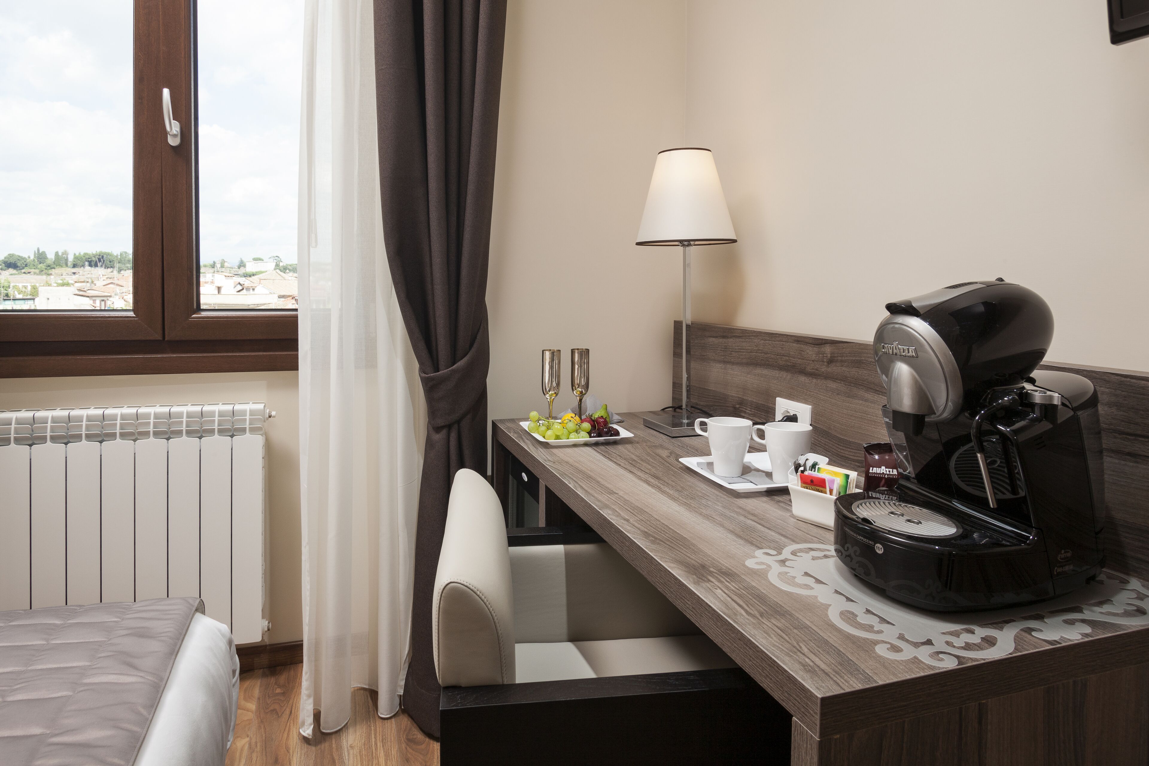 Habitación de hotel con cama, escritorio, cafetera, lámpara y vistas al exterior.