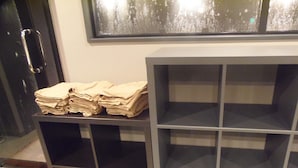 Une pièce avec un meuble noir aux portes vitrées, une pile de serviettes beiges posée sur le dessus, et une fenêtre donnant sur des arbres.