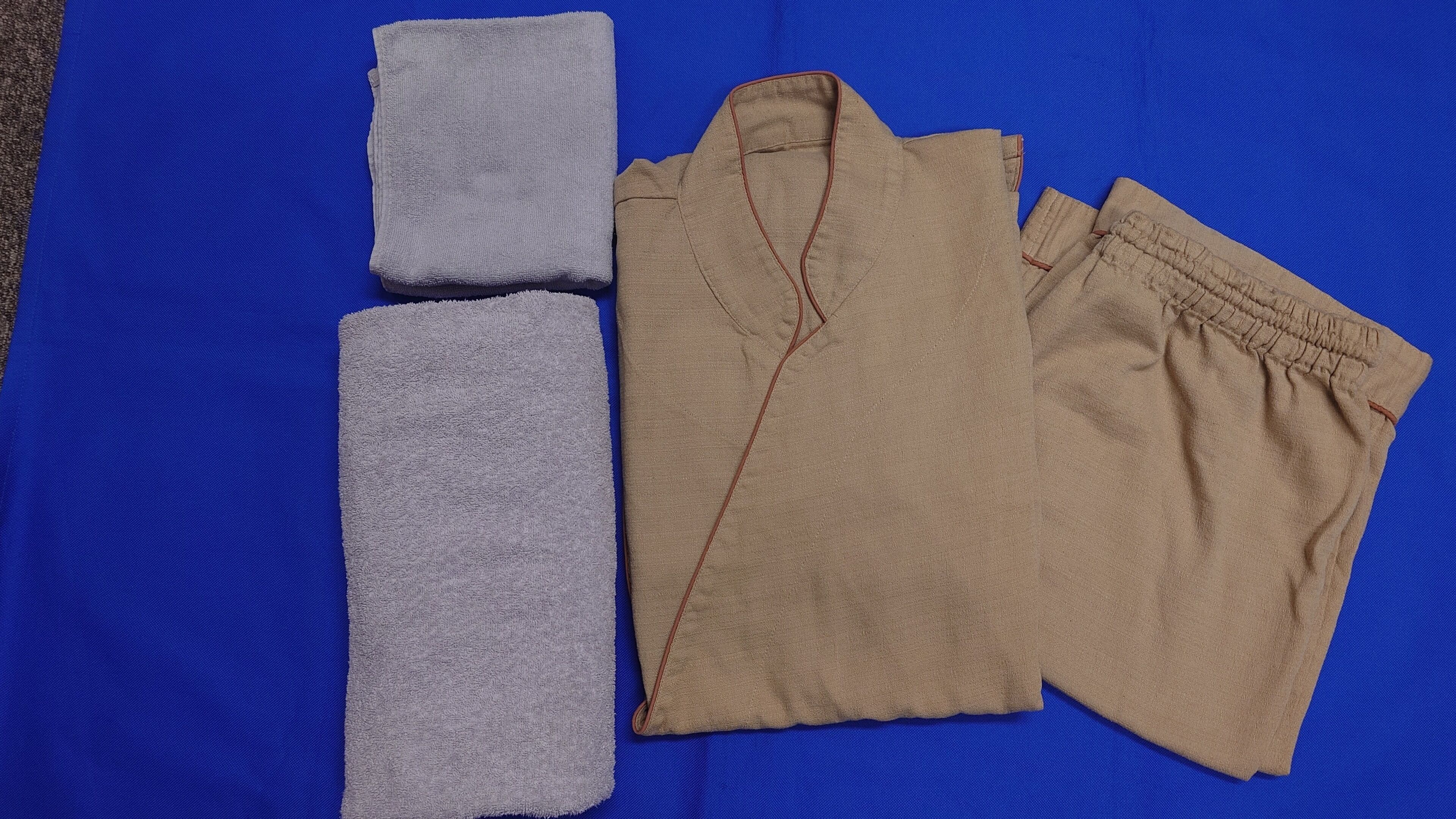 Une surface bleue sur laquelle sont posés un vêtement beige plié et deux serviettes grises pliées.