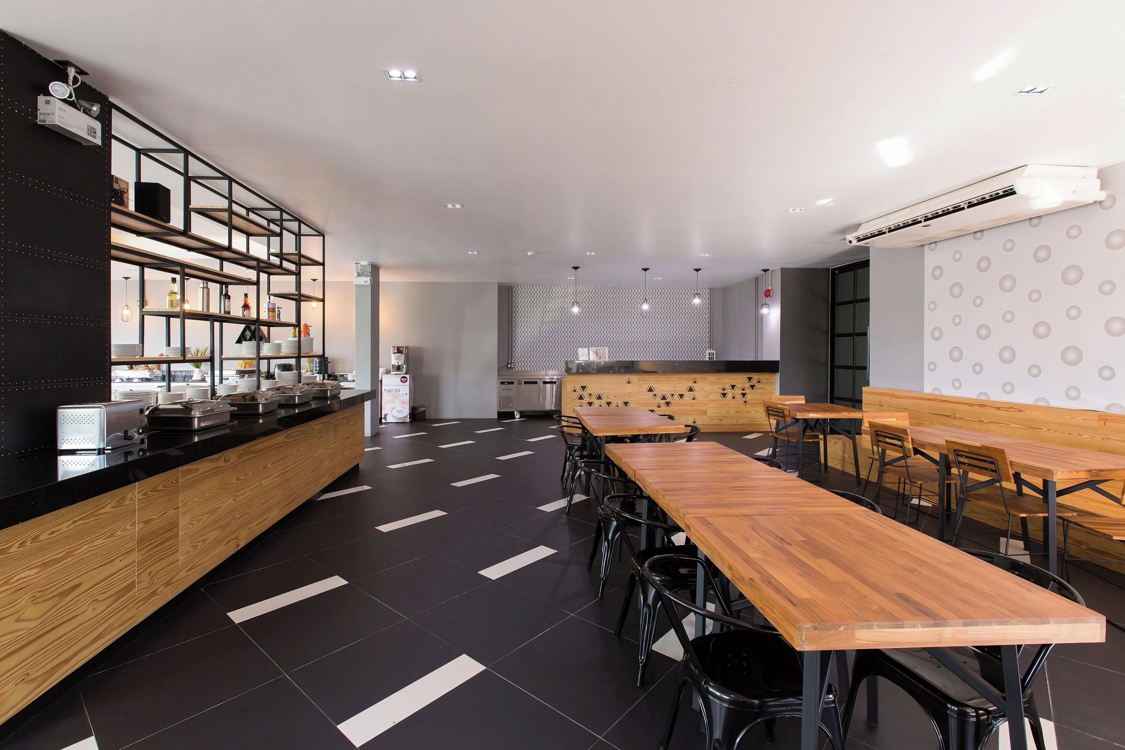 Een modern restaurant met een zwart-wit kleurenschema, met een lange houten toonbank, verschillende zithoeken en een keuken op de achtergrond.