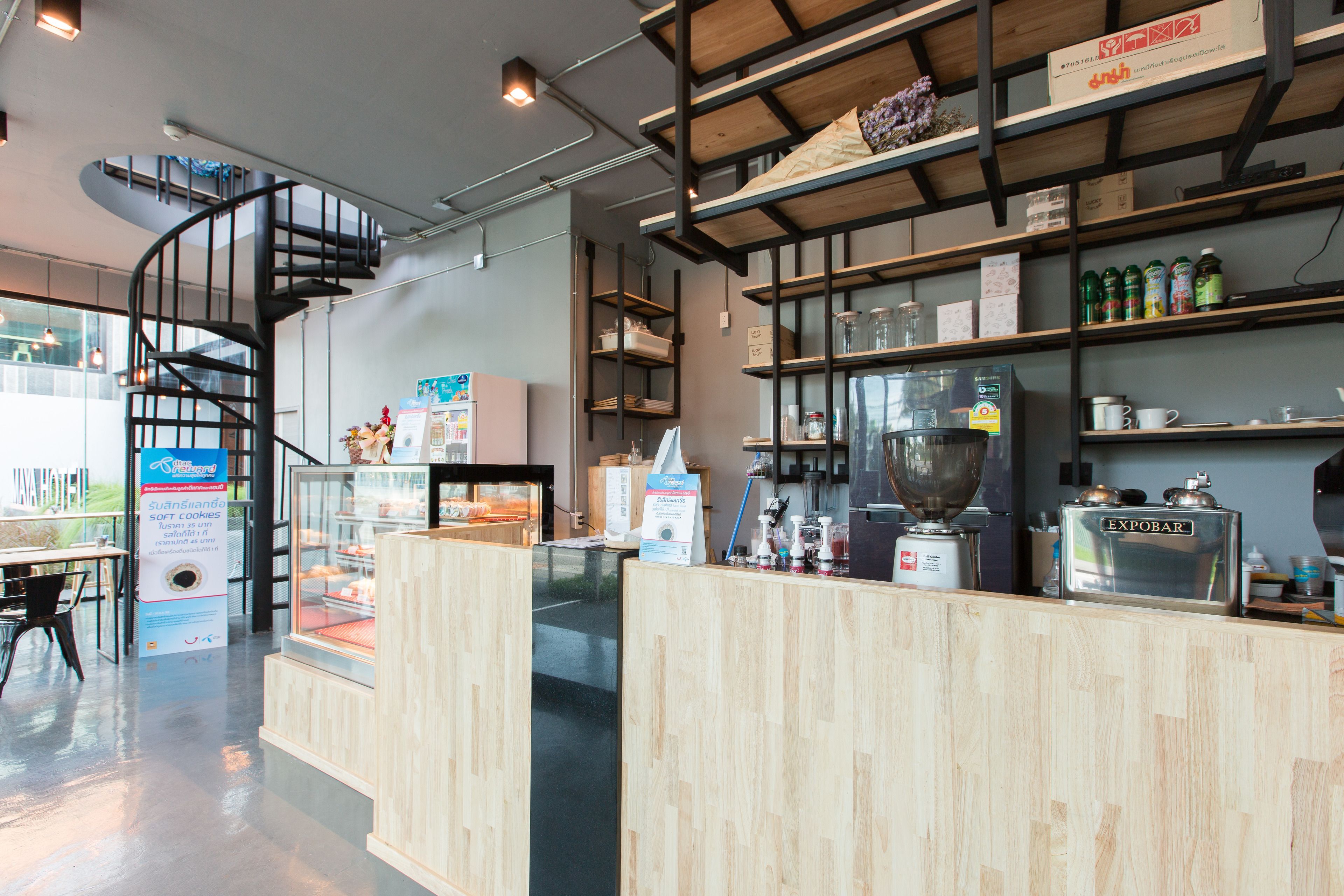 Interior moderno de una cafetería con mostrador de madera, máquina de espresso y una escalera de caracol.