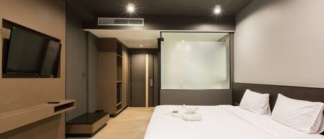 Una habitación de hotel moderna con una cama grande, un televisor de pantalla plana montado en la pared, un equipo de aire acondicionado integrado y una puerta corredera que da al baño.