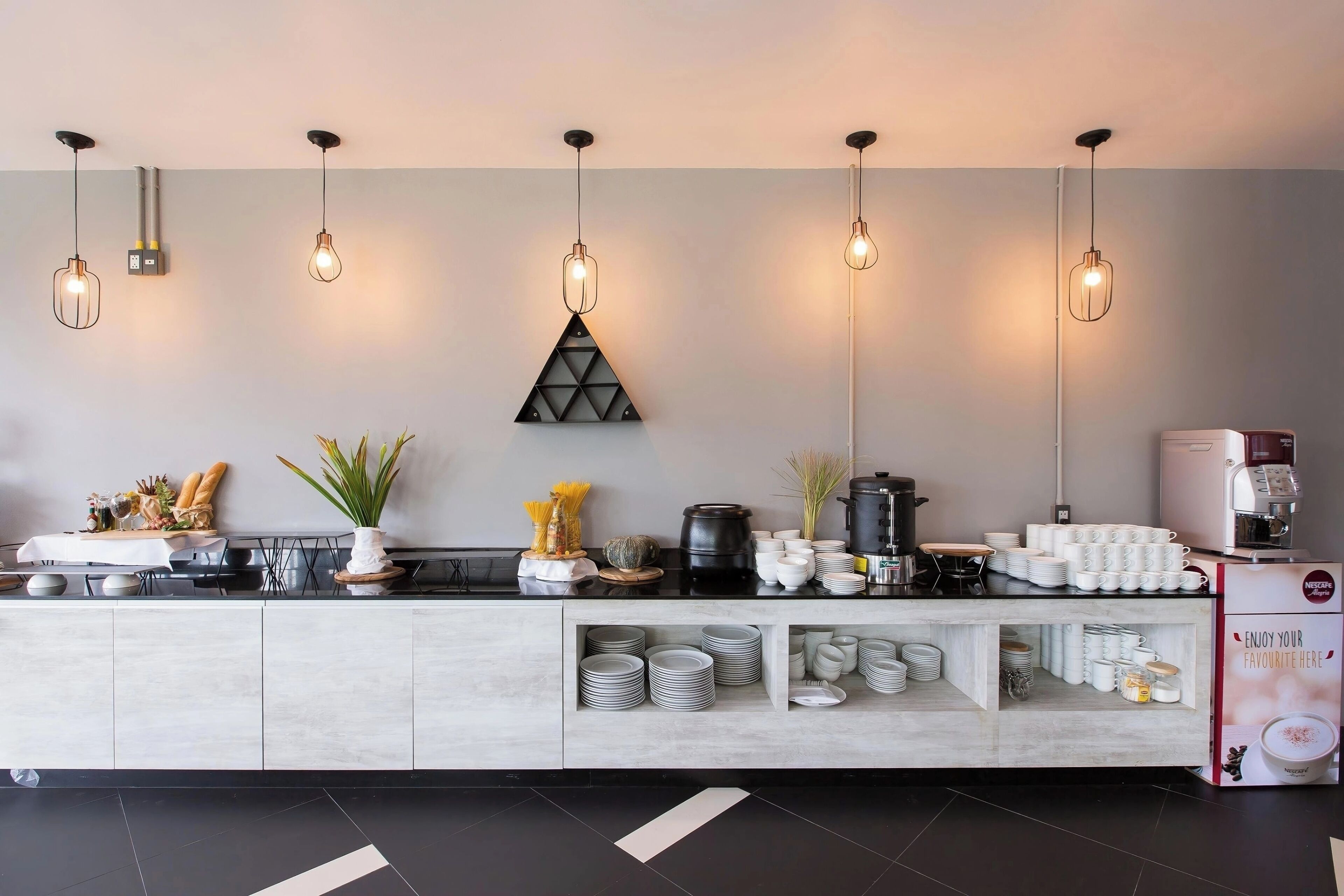 A modern hotel reception area with a long counter, neatly arranged plates, cups, and a coffee machine.