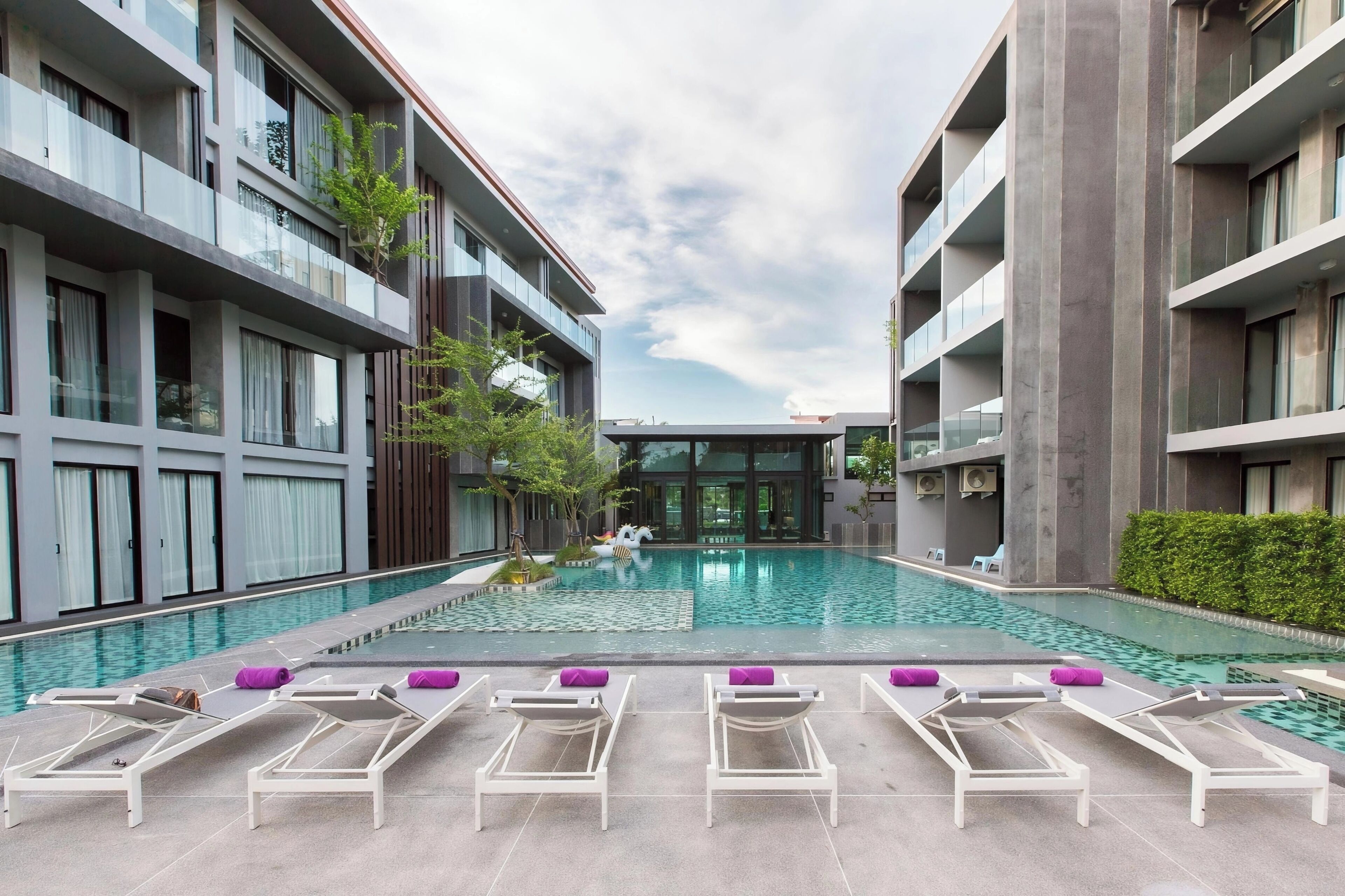 A modern hotel with a central swimming pool, lounge chairs, and a view of the building's interior.